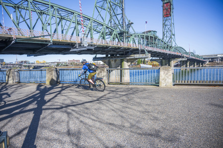 Cyclist pedals a bicycle and rides along the Portland waterfront with bridge, preferring, like most Portland residents, an active healthy lifestyle and an alternative eco friendly mode of transportの写真素材
