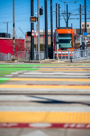 Portland Oregon local transportation streetcar carrying passengers as part of its route stands at a tram stop near a road pedestrian crossing for safe getting off the streetcar and boarding of people