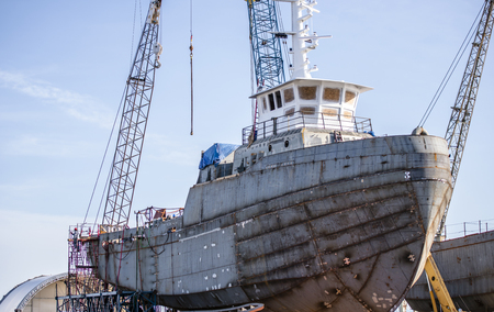 Shipyard on which build a ship or yacht with hold, navigation wheelhouse and cabins welded from sheets of metal mounted on special supports around which construction work continues to be carried outの写真素材