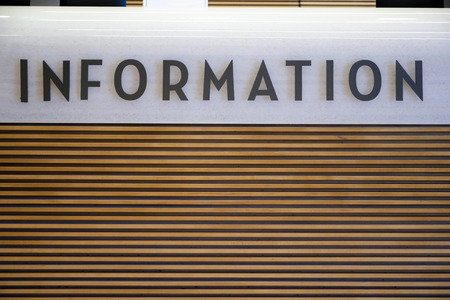 The reception desk is made of natural wooden slats, covered with colorless varnish, and packed horizontally on a frame covered with white granite stone with the sign Informationの写真素材