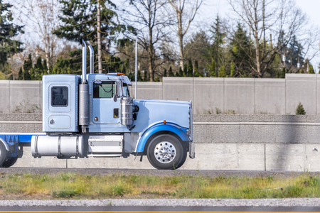 Profile of industrial grade freight transportation big rig blue semi truck tractor with day cab and small sleeping compartment behind running on the road for pick up loaded semi trailer for deliveryの写真素材