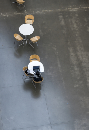 Students of an educational institution study the material studied on their own using laptops with educational programs, sitting at round tables in a university lobby in a free cozy atmosphereの写真素材