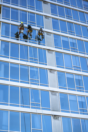 Window washers in special equipment with the necessary tools and detergents, like climbers, descend on the ropes from the roof of a skyscraper, each washes out a certain area of a building windowsの写真素材