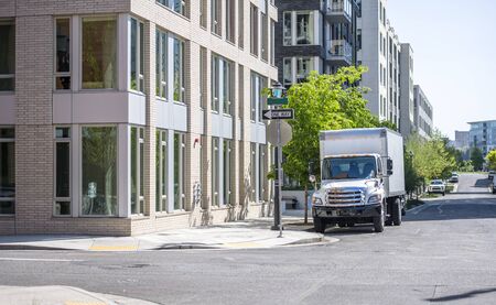 Compact rig semi truck with box trailer for moving to new apartments and local deliveries standing on the city street with multilevel apartment buildings for loading goodsの写真素材