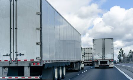 Back view of convoy of the industrial freight transportation of big rig semi trucks with semi trailers running on the wide highway on several lines for delivering commercial cargoの写真素材