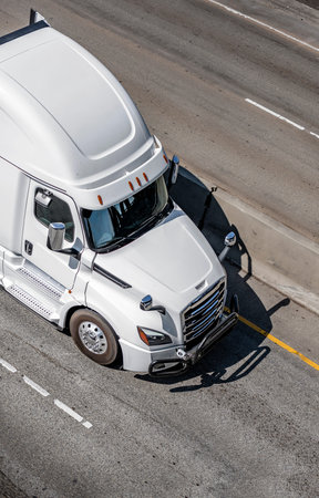 Big rig white bonnet semi truck tractor with grille guard driving on the wide multiline highway road...