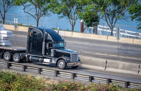 Black big rig American bonnet semi truck with high exhaust pipes transporting stacked covered...