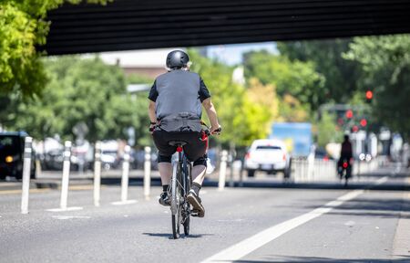 An elderly Man cyclist pedals a bicycle and rides along the Portland down town, preferring like most Portland residents, an active healthy lifestyle and an alternative eco friendly mode of transportの写真素材