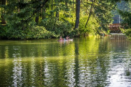 Lovely couple are ride on floating boards on a picturesque Lacamas Lake in the forest and breathing healthy fresh air to strengthen immunity and strengthen the bodyの写真素材