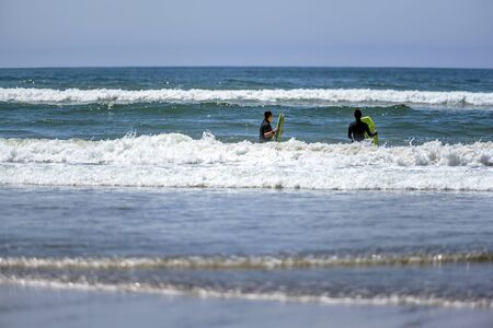 Girls in black thermal jumpsuit who love to ride the waves swim with yellow boards on the waves of the Northwest Pacific Oceanの写真素材