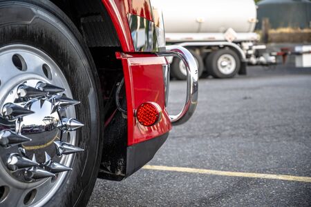 Big rig red heavy-duty powerful semi truck wheel with aluminum rim and shiny tire and chrome grille guard standing on the truck stop parking lot in dedicated spotの写真素材