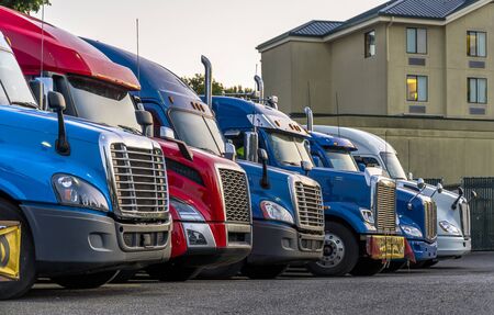 Different make and models big rigs semi trucks with semi trailers standing in row on truck stop parking lot for rest and comply with the movement according to the schedule for successful deliveryの写真素材