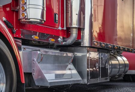 Big rig red heavy-duty powerful red semi truck with lot of chrome accessories and aluminum footboard standing on the truck stop parking lot in dedicated spotの写真素材