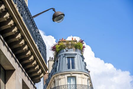 Rounded cone residential apartments multi-storey house with wooden shutters and residential attic and balconies and plants on the roof located on one of the streets of Paris with old buildingsの写真素材