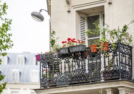 Residential multi-storey apartments house with wooden shutters and metal balcony with flowers in flowerpots and street lamp on the wall located on one of the streets of old Paris with old buildingsの写真素材