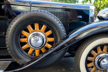 Elegant stylish black old vintage retro car with large convex wings and chrome headlights and wheels with wooden spokes on an improvised street exhibition of retro cars in a provincial townの写真素材