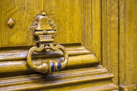 Fragment of old yellow painted wooden door with a peeling paint and forged metal handle doorknob as a symbol of communication and protection of private interests and safe personal life informationの写真素材