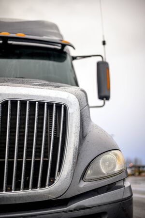 Front of dark gray big rig semi truck with efficient eco-friendly diesel engine and chrome grille with rain drops standing on the industrial parking lotの写真素材