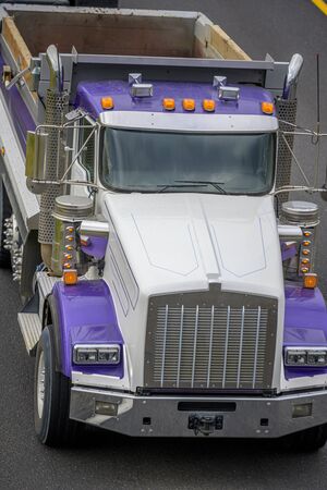 Big rig colored heavy-duty local haul day cab diesel tipper truck with vertical exhaust pipes with empty dump trailer running on the road with marked lines to point of work for loadの写真素材