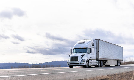 Powerful long haul big rig industrial grade diesel semi truck transporting commercial food cargo in refrigerated semi trailer running on the flat road with sky and hills view in Columbia Gorgeの写真素材