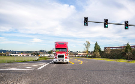 Bright red big rig powerful classic American long haul semi truck with grille guard driving on the...