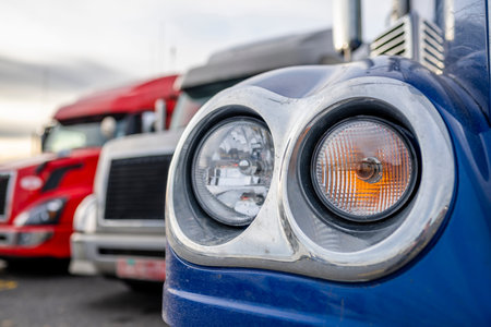 Different big rigs semi trucks with semi trailers standing in row on truck stop parking lot with...