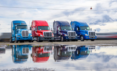 Powerful clean big rigs semi trucks tractors with high cab and rest compartment for truck drivers resting standing on the warehouse parking lot waiting for loaded semi trailer for next deliveryの写真素材