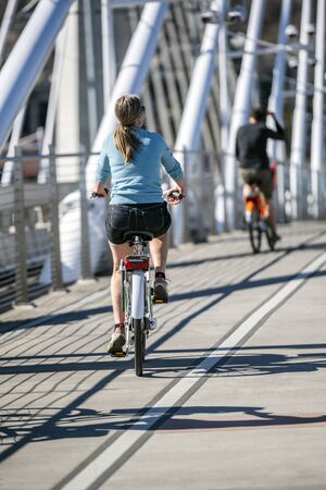 A Slender girl on a bike pedals a bicycle on the Tilikum Crossing Bridge preferring an active healthy lifestyle using cycling ride and cycle as an alternative environmentally friendly transportationの写真素材