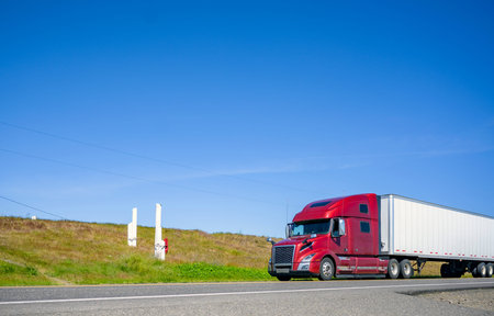 Big rig bonnet long haul burgundy diesel semi truck transporting commercial cargo in dry van semi...