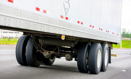 Powerful big rig semi truck transporting loaded commercial cargo in white long dry van heavy-duty...