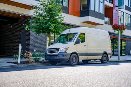 Compact cargo mini van for delivery and small business services standing on the urban city street with urban multi level residential apartment buildingの写真素材