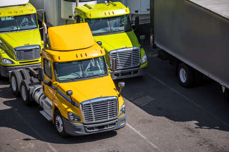 Medium duty professional freight powerful rigs industrial diesel semi trucks with refrigerated semi trailers standing on the tight warehouse street parking lot waiting for the next deliveryの写真素材