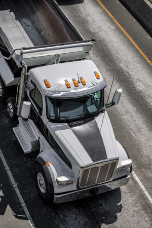 Big rig black and white industrial grade powerful professional tipper semi truck tractor with empty dump trailer running on the marked road to point of destination for next loadの写真素材