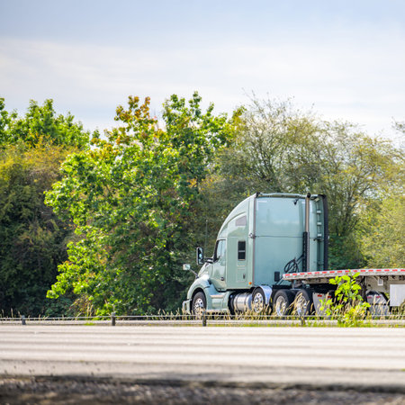 Light green long hauler big rig red industrial semi truck transporting empty flat bed semi trailer...