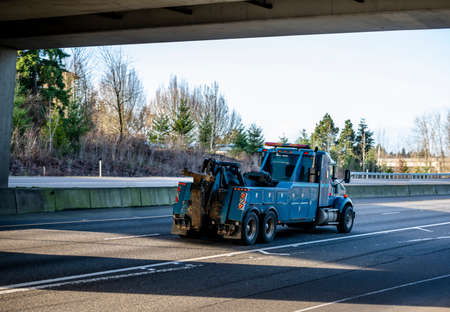 Classic big rig blue semi truck day cab tow tractor with with boom and other towing equipment moving on the highway road intersection with one way traffic direction at sunny day to the accident siteの写真素材