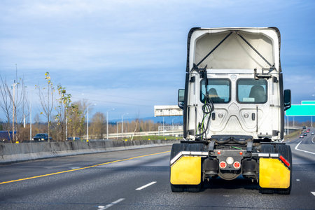 Powerful Big rig white high cab semi truck tractor without semi trailer running on the multiline divided wide highway road to warehouse for pick up the next loaded trailer for deliveryの写真素材