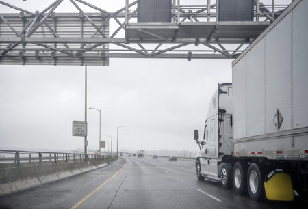 Commercial big rig white semi truck transporting cargo in dry van semi trailer running on the wide...