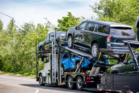 White compact big rig industrial car hauler semi truck transporting cars on the hydraulic modular two level semi trailer running on curving highway road with green mountain forest in Columbia Gorgeの写真素材