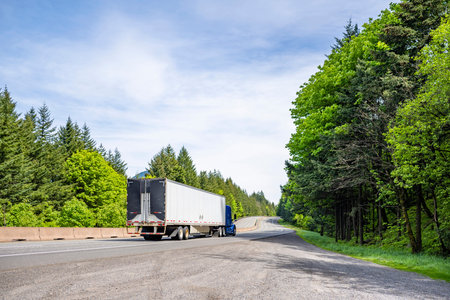 Blue big rig industrial semi truck tractor with roof spoiler transporting cargo in dry van semi...