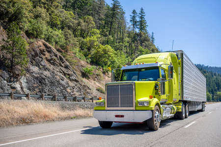 Bright lime stylish industrial grade long haul Big rig bonnet semi truck transporting frozen commercial cargo in refrigerator semi trailer running for delivery on the one way multiline highway roadの写真素材