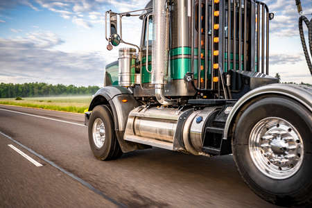 American idol green classic day cab big rig semi truck with turned on light on the cab back protection wall and chrome parts transporting semi trailer driving on the one way highway roadの写真素材
