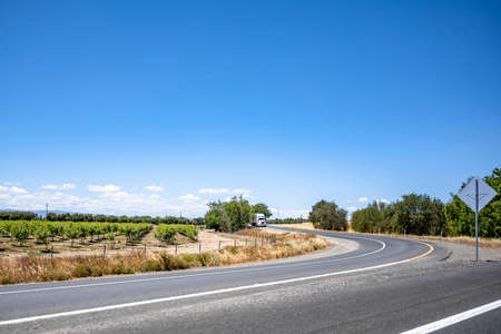 White big rig semi truck tractor caring commercial cargo on dry van semi trailer standing on the shoulder of the highway exit intersection road take a break for truck driver rest in Californiaの写真素材