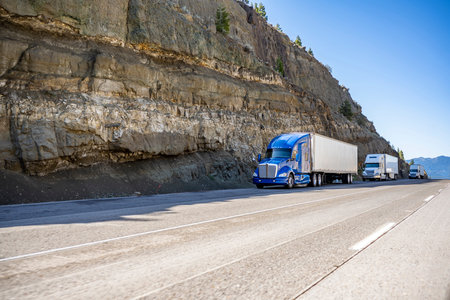 Group of big rigs semi trucks tractors transporting cargo in different semi trailers standing off...