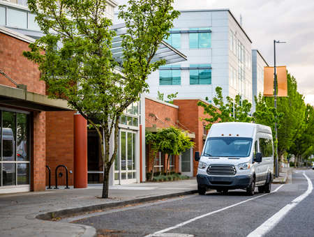Compact industrial small size white mini van with high roof for comfort local delivery and small business needs standing on the urban city street with multilevel apartments buildingsの写真素材