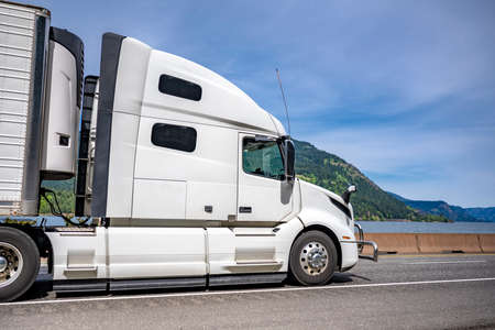 Industrial long hauler big rig white semi truck tractor carrier transporting commercial cargo in refrigerator semi trailer running on the winding highway road along Columbia river in Columbia Gorgeの写真素材