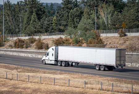 Industrial white classic bonnet professional big rig semi truck with truck driver rest compartment transporting frozen commercial cargo in reefer semi trailer running on the summer highway roadの写真素材