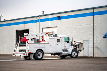 White powerful semi truck equipped with crane and welding machine for mobile repair of broken vehicles on the road stands with an open hood in a parking lot near a warehouse for maintenanceの写真素材