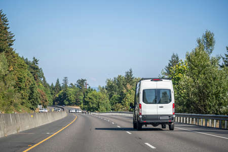 Compact industrial small size white mini van with cargo compartment for local deliveries and small business needs running on the wide multiline highway road for customers commercial cargo deliveryの写真素材