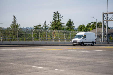Compact industrial small size white mini van with cargo compartment for local deliveries and small business needs running on the wide multiline highway road for customers commercial cargo deliveryの写真素材