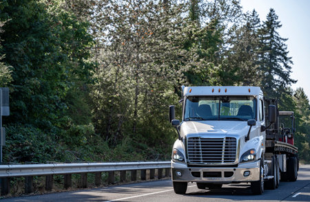 Day cab bonnet white industrial semi truck tractor transporting cargo on flat bed semi trailer running on the one way highway road to warehouse for timely delivery at twilight timeの写真素材